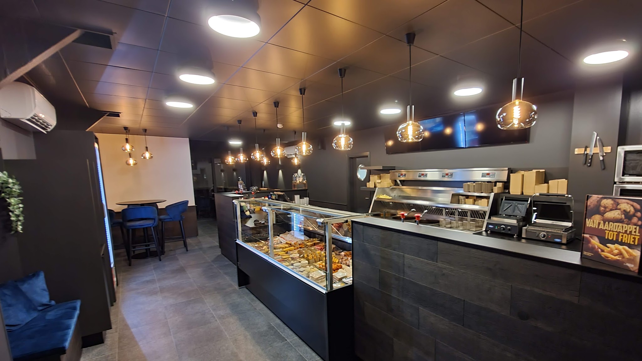 Het interieur van @ The Yumm: lange donkere toog, snackvitrine en hanglampen