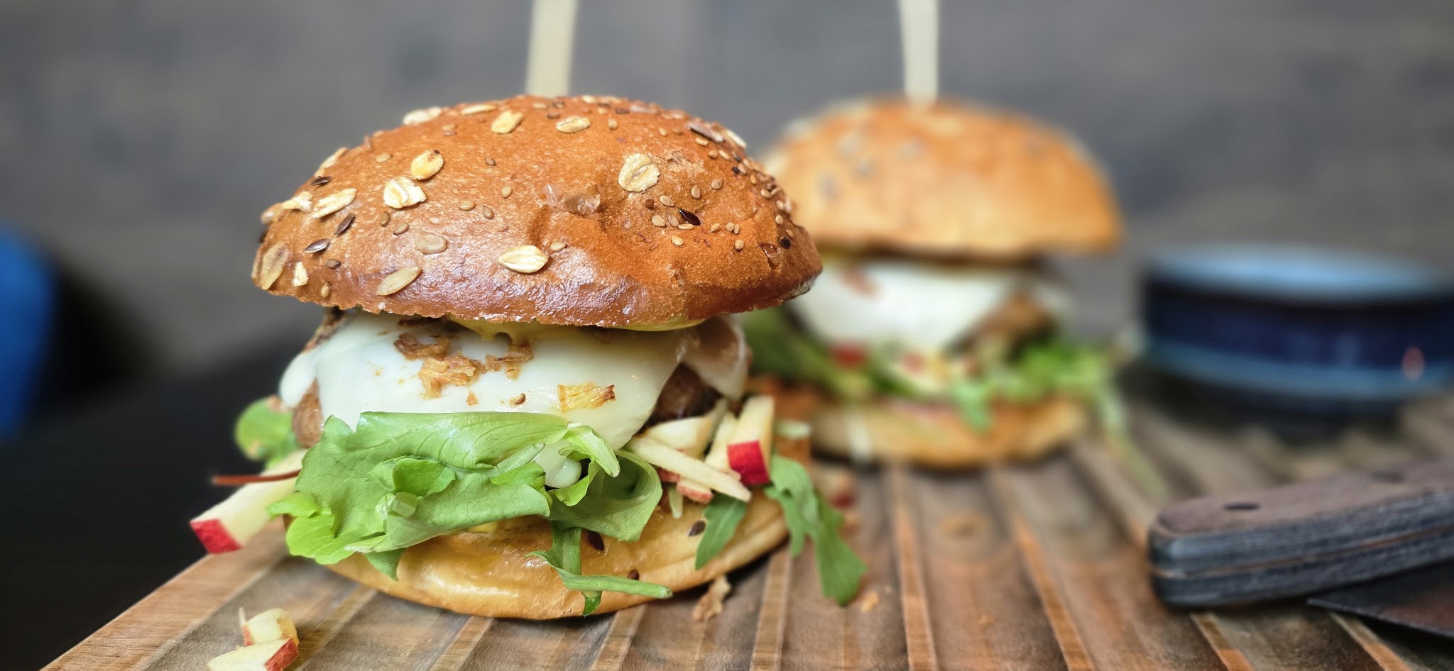 Twee huisgemaakte burgers met sla, appel en kaas op een houten plank