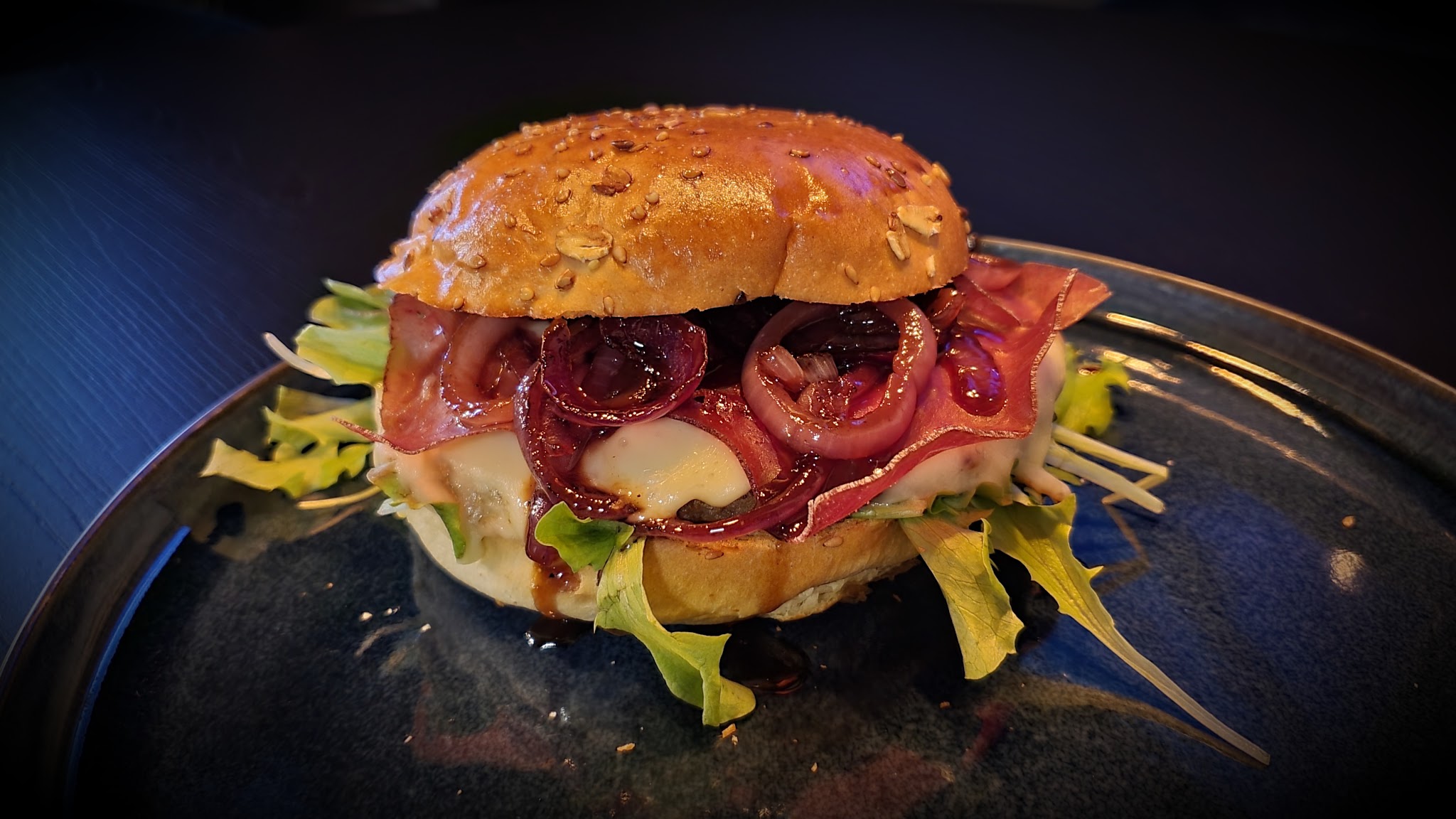 Huisgemaakte burger met rode ui, ham, kaas en frisse sla op een donkerblauw bord