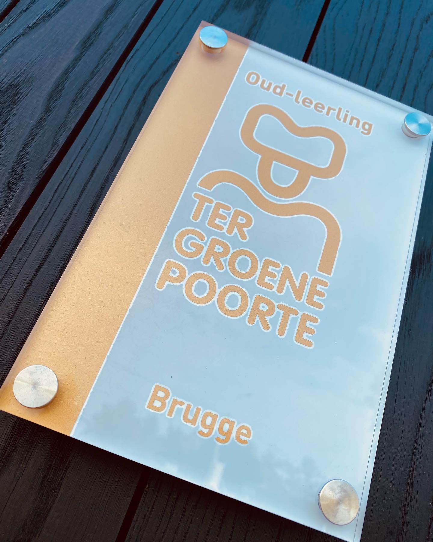 Plaatje ‘Oud-leerling Ter Groene Poorte Brugge’ op een donkere houten tafel